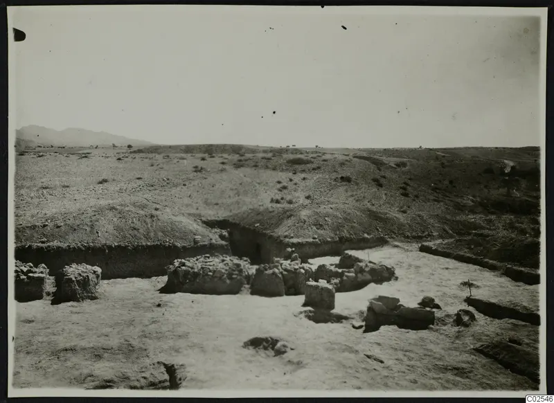 Excavated area at Ayios Iakovos with low stone walls and an earth bank, under a wide open sky.