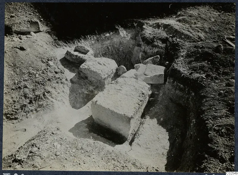 Excavation at Marion, T.86, with large pale stone blocks lying in a dug pit and grass along the edges