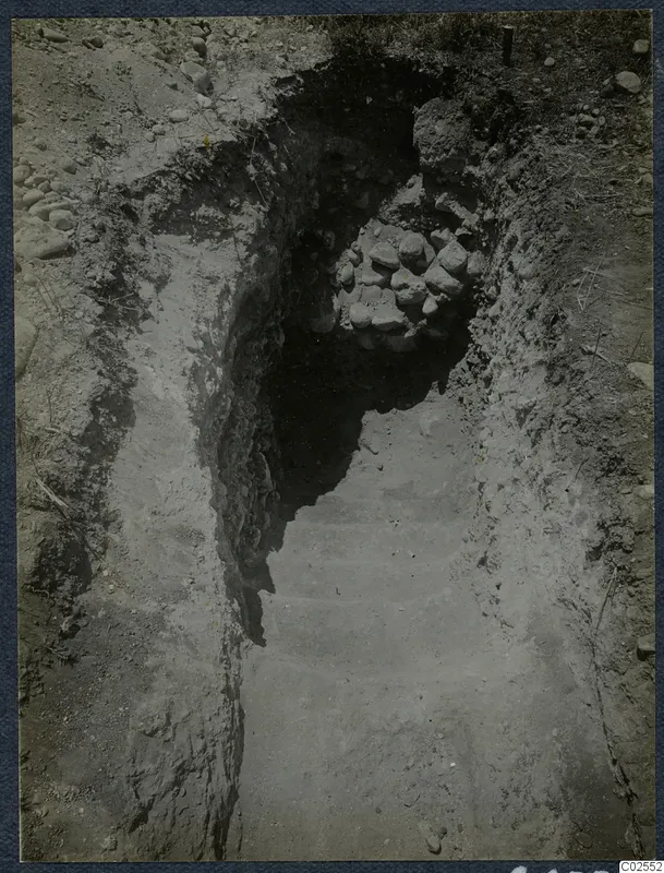 Excavation cutting at Marion, T.92, sloping down toward a heap of stones at the far end, with grass and stones on the ground
