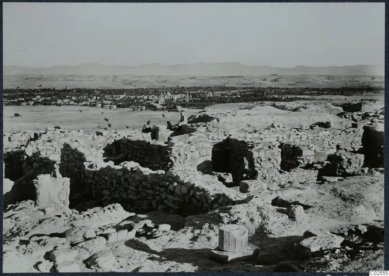 Ruined stone walls of the acropolis at Idalion, with a town, trees and hills in the distance.