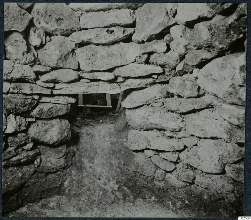 Tomb chamber at Enkomi during excavation, with walls of stacked stones and a wooden frame in the far opening.