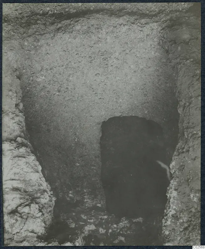 Excavated cutting with rough earth walls leading down to a dark tomb entrance at Enkomi