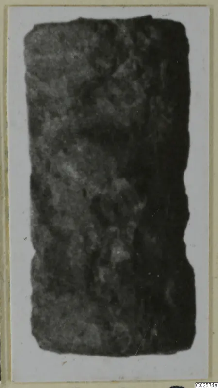 Dark cylindrical seal, photographed on a card mount, with faint markings across its surface