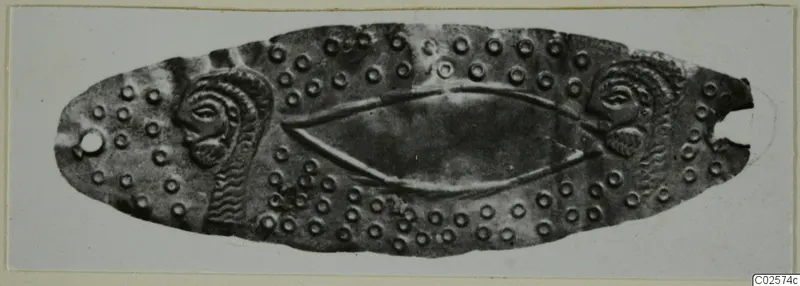 Embossed metal mouthpiece from Enkomi: an elongated oval plate with spiral motifs at each end and small raised rings across its surface.