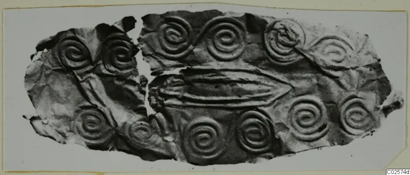 Fragment of thin metal sheet with embossed spirals and a central raised ridge, recorded as a mouthpiece