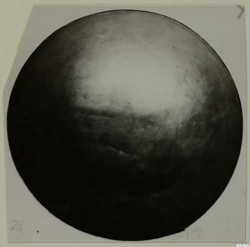 Round dark object with a glossy highlight, photographed on a pale grey card mount
