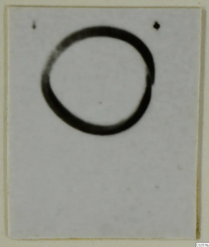 Blurred photograph of a ring-shaped object on a pale card background