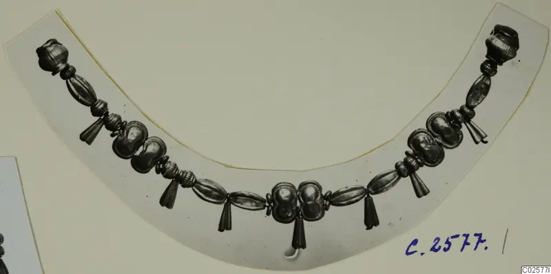 Curved necklace of metal beads with tassel-like pendants, photographed on a pale card.