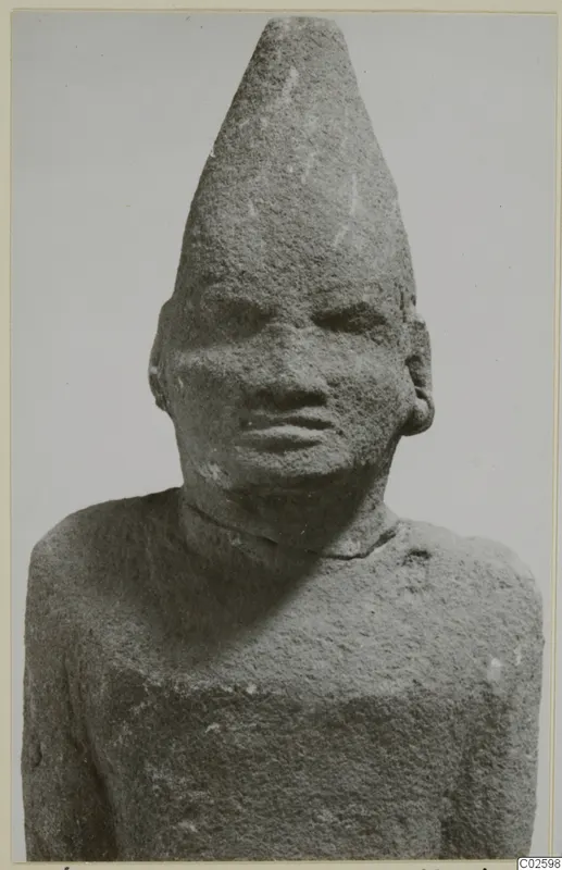 Limestone Cypro-Egyptian sculpture of a head and upper torso with a tall conical cap, seen from the front.