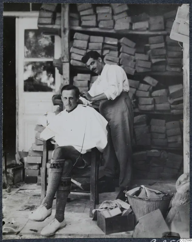 Man in a white cape having his hair cut indoors, in front of stacked wooden boxes.