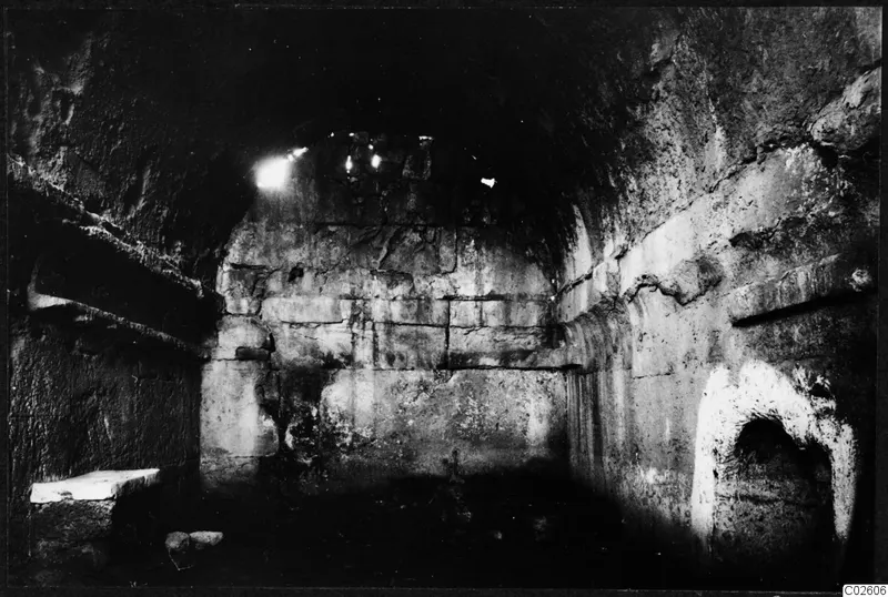 Interior of a built tomb chamber with a stone bench on the left and an arched niche in the right wall