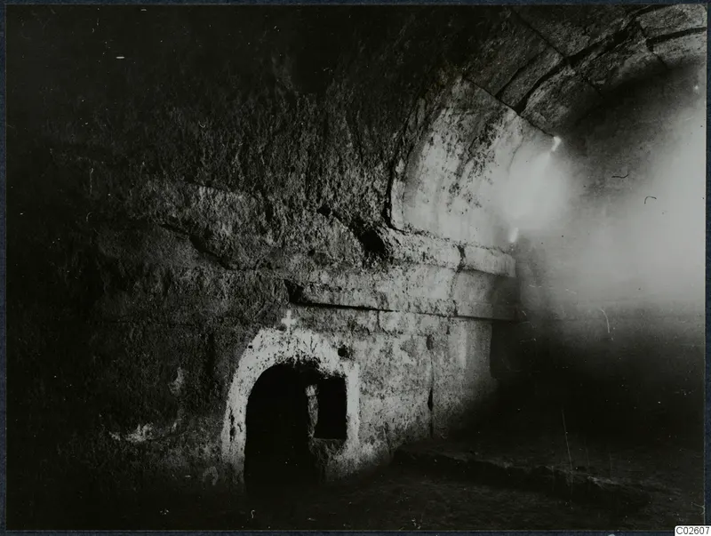 Interior of a built tomb with a stone vault and a low arched doorway in the wall