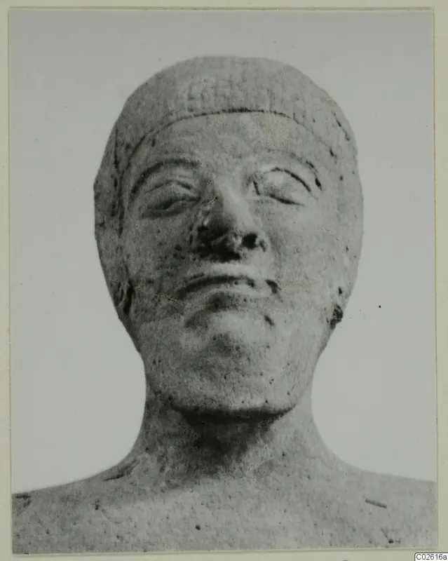 Frontal view of a carved head and upper shoulders with a broad band across the brow, against a plain background.
