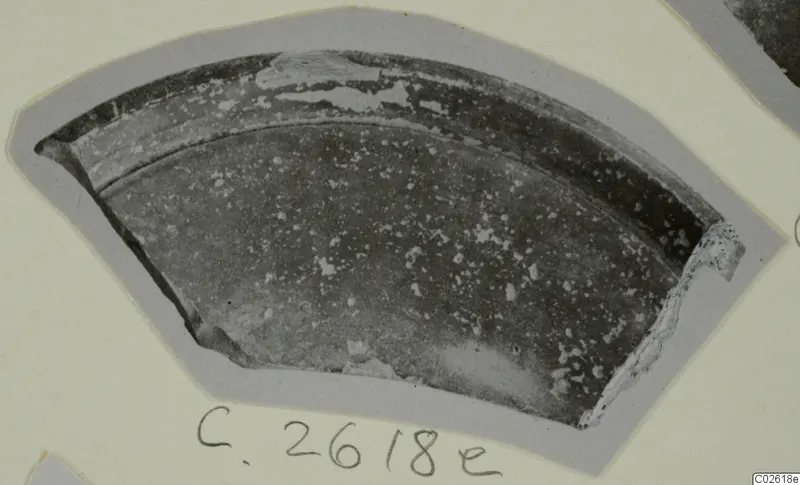 Curved pottery sherd with a dark surface and pale flaked patches, photographed on a card with a handwritten number label