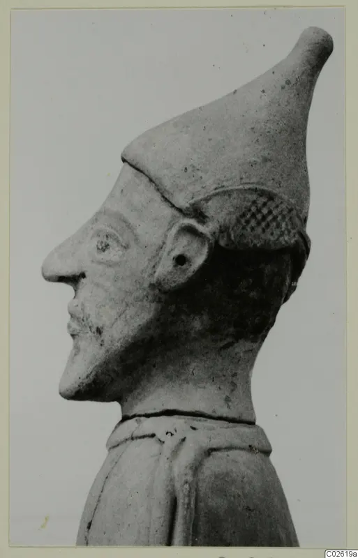 Terracotta figure in profile facing left, with a tall conical cap and a cross-hatched band beside the head.