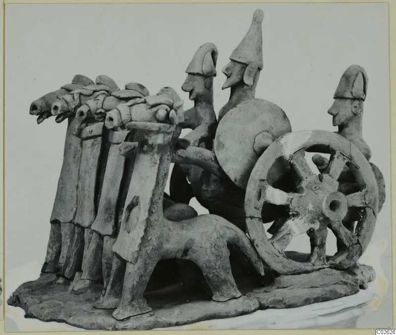 Terracotta model of a chariot drawn by horses, with three figures and a spoked wheel, on a flat base.