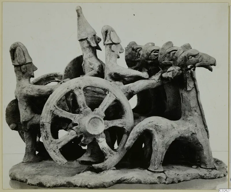 Terracotta model of a chariot with a large spoked wheel, human-like figures and animal forms on a flat base.