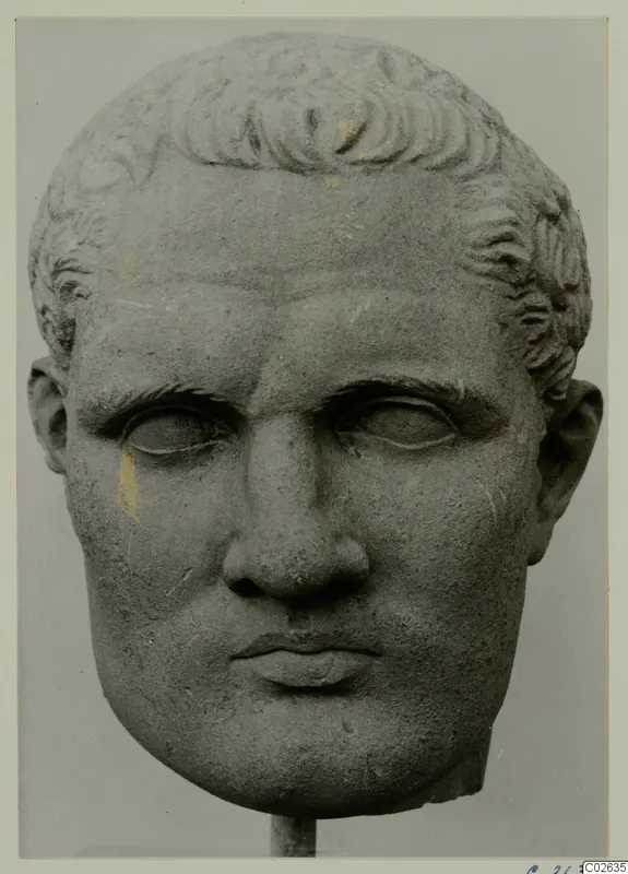 Stone sculpture head of a man with short curled hair, mounted on a stand