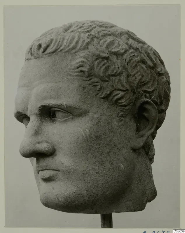 Carved stone head of a man with short curly hair, shown on a thin rod stand.