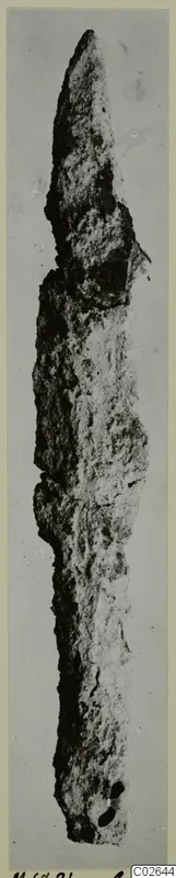 Corroded iron spearhead, a long narrow blade tapering to a point, with two small holes near the lower end.
