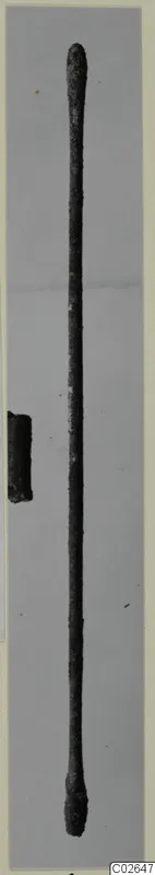 Long slender metal rod with thickened ends and a short fragment beside it, photographed on a grey background