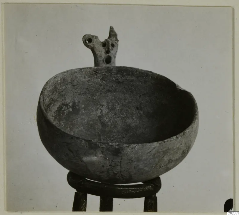 Black Slip Ware bowl with a pierced projection on its rim, shown on a ring-shaped stand