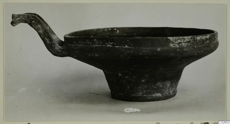 Dark pottery bowl on a tall foot, with a long handle curving up from its rim, from Ayios Iakovos