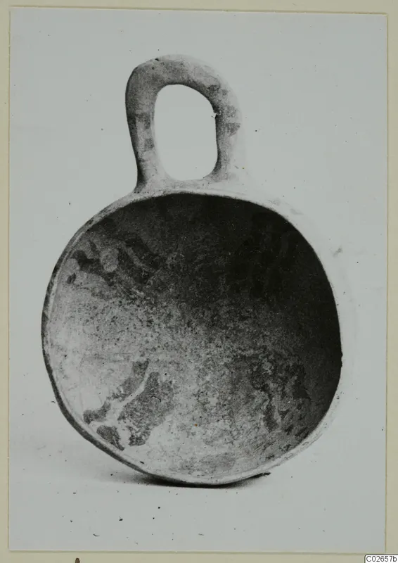 Pottery bowl with a loop handle, interior showing dark painted decoration on a pale surface.
