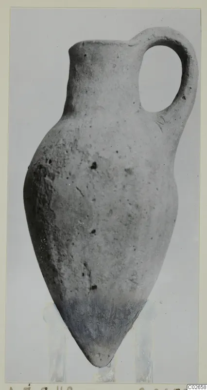 Pottery bottle with a single loop handle and pointed base, photographed against a plain grey background.