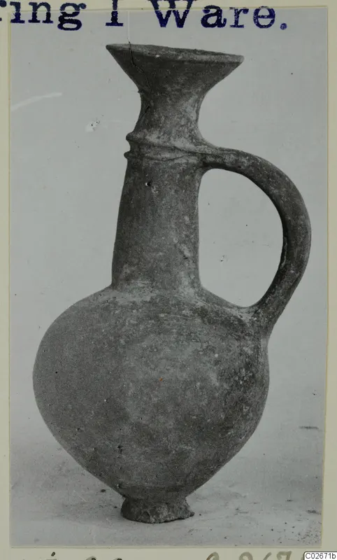 Juglet of Base-Ring Ware with a flaring mouth, strap handle and ring base, photographed on a plain background