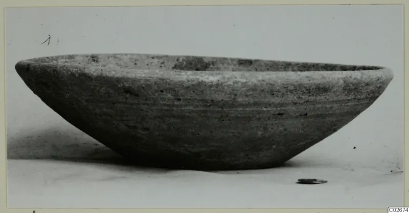 Wheel-made plain bowl with a wide, shallow body, photographed from the side on a pale surface.