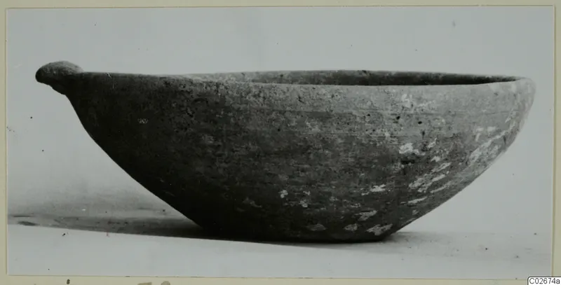 Plain white wheel-made bowl with a small handle projecting from the rim, seen from the side