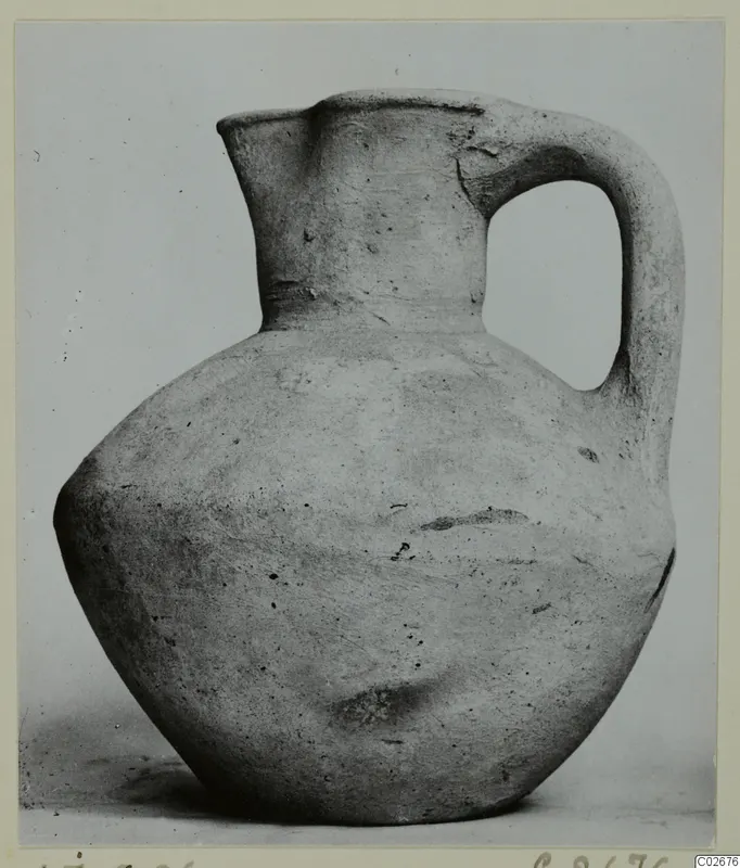 Pottery jug, plain white wheel-made, with one strap handle and a pinched spout, photographed against a plain backdrop