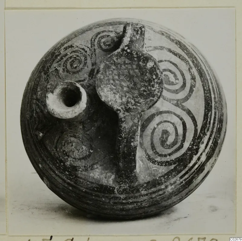 Painted stirrup jar from Ayios Iakovos with a spout and strap handle, decorated with dark spirals and bands.