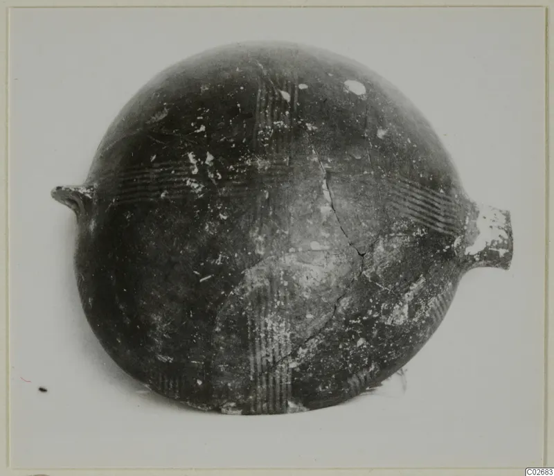 Round-bodied pottery vessel with two small lugs and incised parallel-line bands, photographed on a pale background.