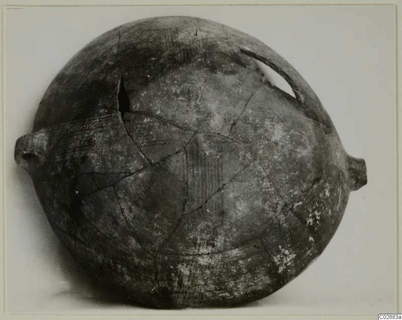 Globular pottery vessel with side lugs and a broken loop handle, reconstructed from sherds, shown against a pale background.