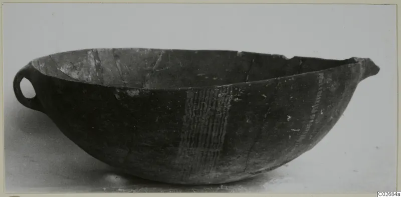 Deep bowl with a small loop handle and pale vertical hatched bands on its dark body, seen in profile