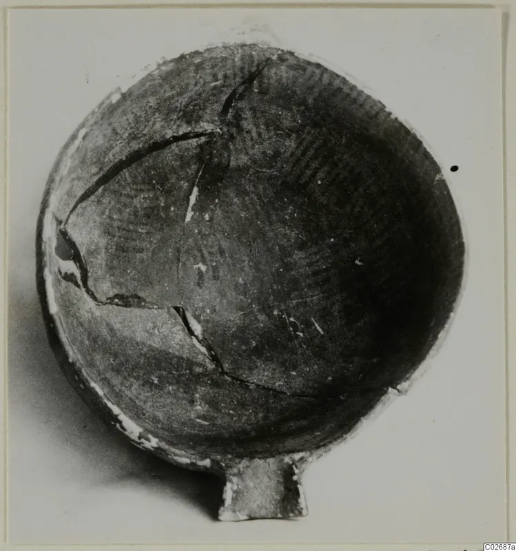 Pottery bowl with a small handle, seen from above, with cracks across its dark surface