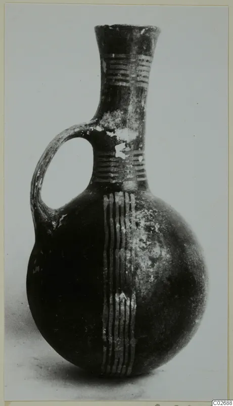 Dark jug with a single loop handle, a flaring neck and pale painted bands on the neck and body.