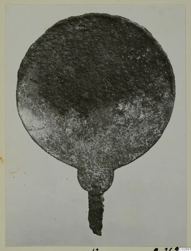 Corroded round metal disc with a narrow tang, photographed on a mounted card; from Marion Tomb 14