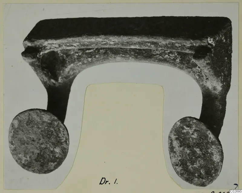 Corroded metal object from Marion with a flat top bar, a curved underside and two round discs at its ends