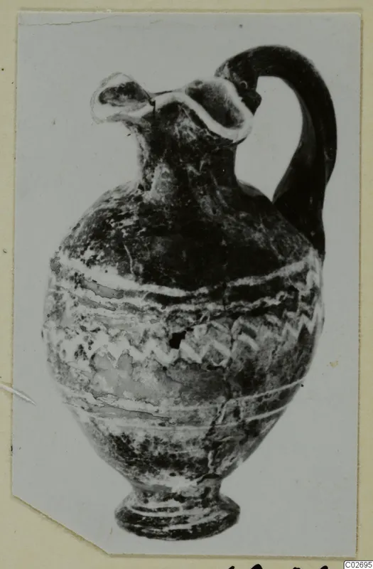 Black-glazed juglet with a trefoil mouth, a single strap handle and white painted bands and zigzag pattern on the body.