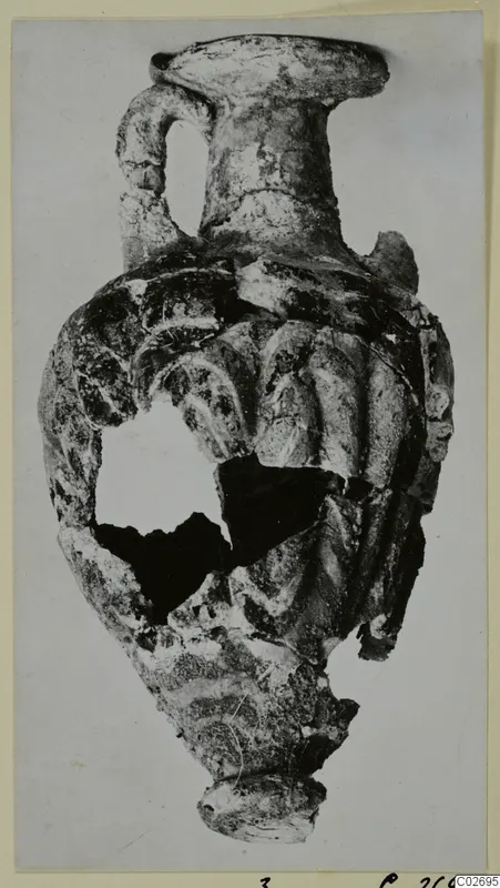 Sand-core glass amphoriskos from Marion Tomb 7, with a ribbed body and a loop handle on one side.