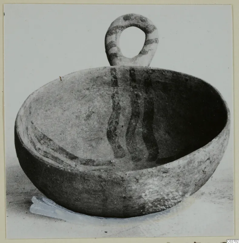 Pottery bowl with a looped handle and painted bands, photographed on a light background.