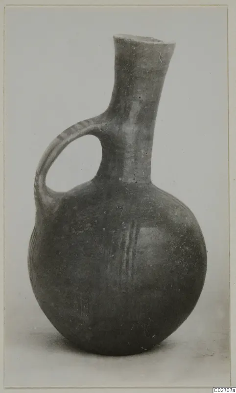 Round-bodied jug with a tall neck and a loop handle, dark surface with a few pale painted lines