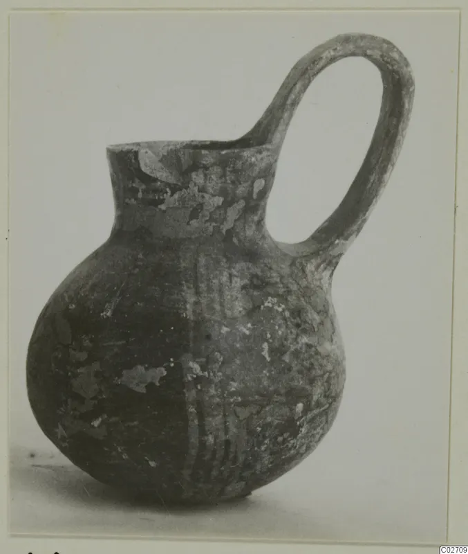 Red-on-Black pottery jug with a tall loop handle, photographed against a plain pale background