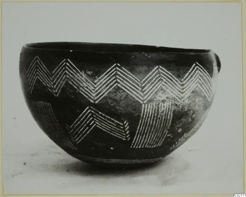 Dark polished bowl with white-painted zigzag and hatched bands, photographed against a pale background.