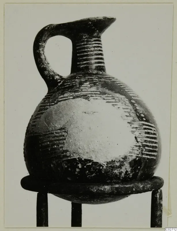 Pottery jug from Lapithos with a strap handle, grooved neck and globular body, on a metal stand