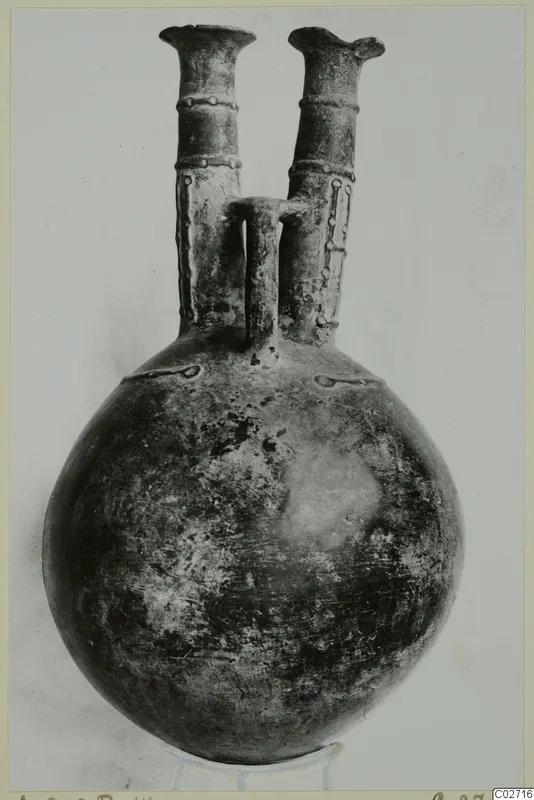 Pottery jug with a round body and two tall flared necks joined by a central handle, photographed on a stand.