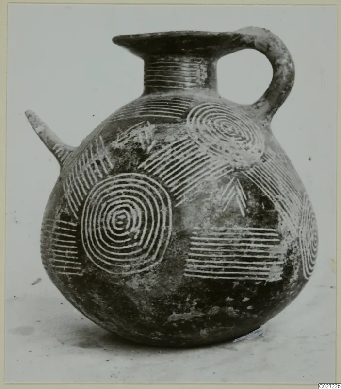 Dark polished jug with a side spout, a loop handle and incised concentric circles and bands on its body